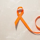 Cinta naranja sobre fondo de mármol claro, símbolo de la concienciación sobre la violencia de género y la salud mental.