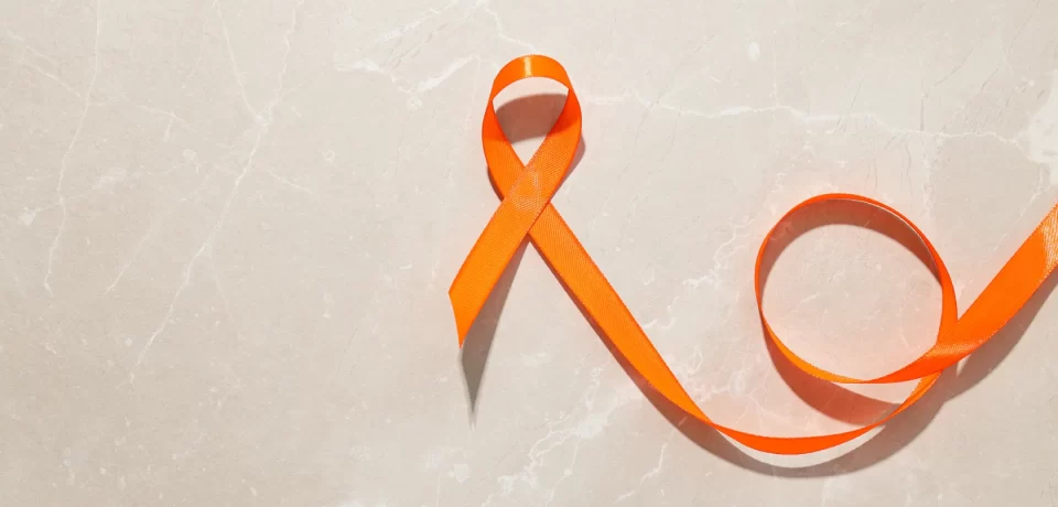 Cinta naranja sobre fondo de mármol claro, símbolo de la concienciación sobre la violencia de género y la salud mental.
