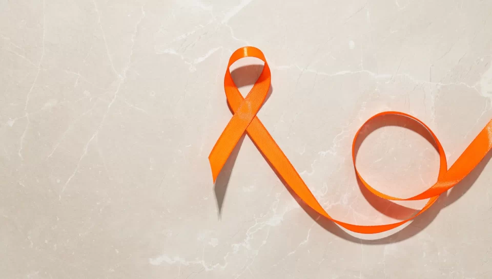 Cinta naranja sobre fondo de mármol claro, símbolo de la concienciación sobre la violencia de género y la salud mental.
